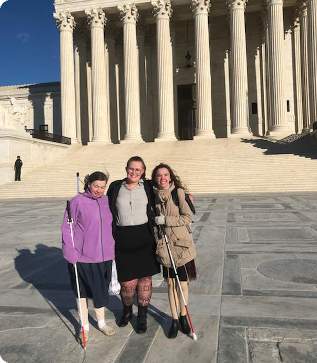 Three blind woman smile together in front of a government building